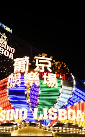 Bright neon signs in multiple colors illuminate the night, prominently displaying the name 'Casino Lisboa' alongside signage in Chinese characters. The lights form intricate patterns and vibrant displays, creating a lively and energetic atmosphere.